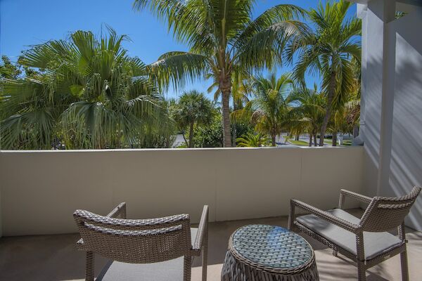 Two chairs and a small table are on a patio with a view of palm trees and a clear blue sky, creating a relaxing outdoor space.