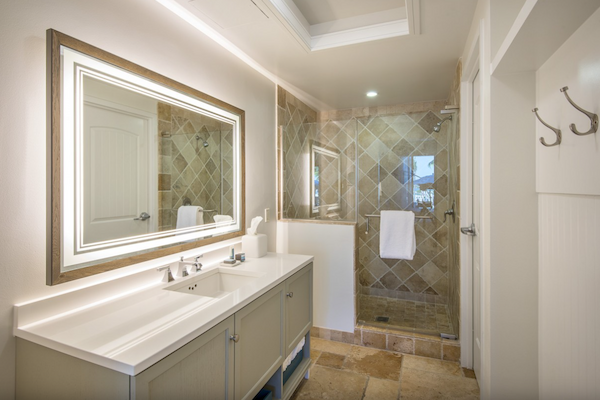 This image shows a modern bathroom with a double sink vanity, large illuminated mirror, and a glass-enclosed shower with tile walls and floor.