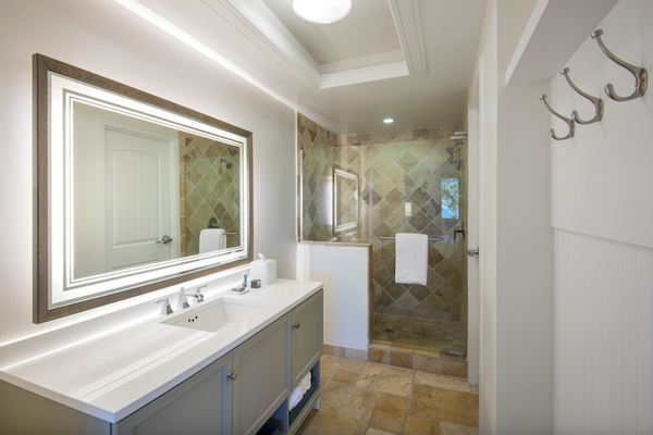 A modern bathroom featuring a large mirror, double sink vanity, and a walk-in shower with a glass enclosure and tiled walls; hooks on the wall.