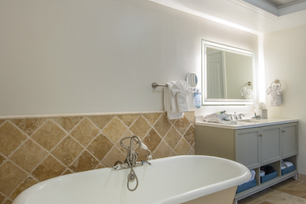 A bathroom with a freestanding bathtub, tile flooring, a vanity with a large mirror, and overhead light fixtures.