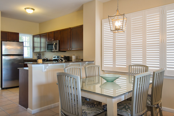 A kitchen and dining area with stainless steel appliances, dark wood cabinets, a glass table with chairs, and a decorative light fixture.