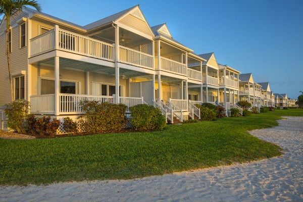 A row of beachside houses with porches, green lawns in front, and a sandy area leading to the beach appears in this image.