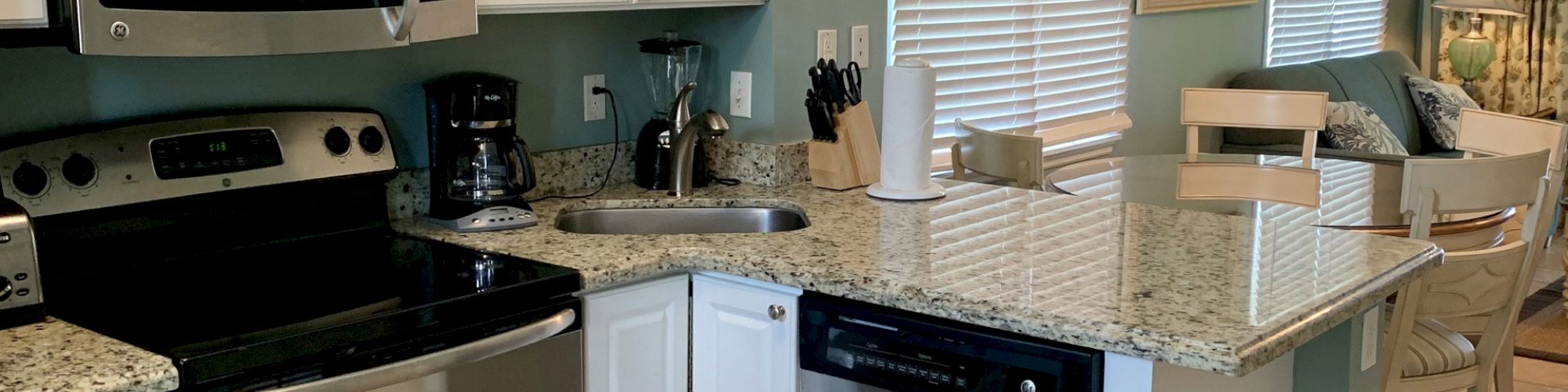 This image shows a modern kitchen with stainless steel appliances, a granite countertop, a sink, and various kitchen tools.