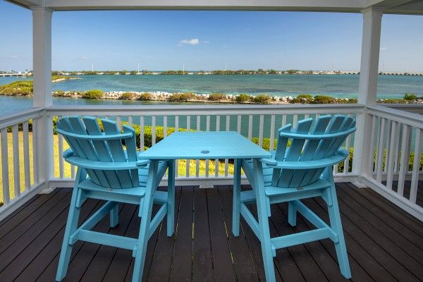 A deck overlooking a body of water, featuring two blue chairs and a matching blue table in the center of the image.