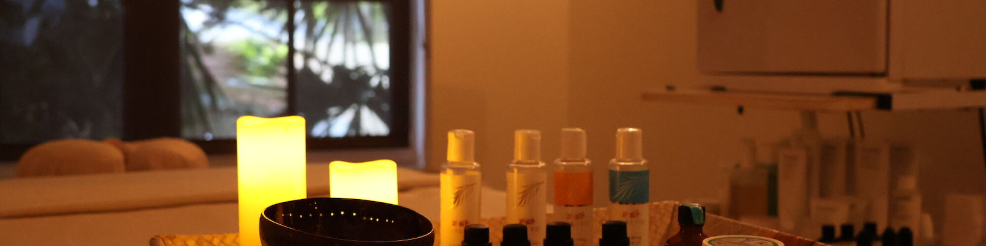 A dimly lit spa setting with candles, essential oils, and sprays on a tray, creating a relaxing ambiance.