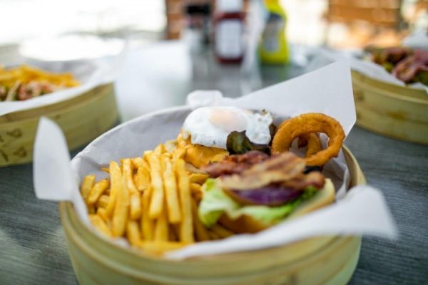 A basket with a burger topped with a fried egg, onion rings, bacon, lettuce, and a side of French fries on a table.