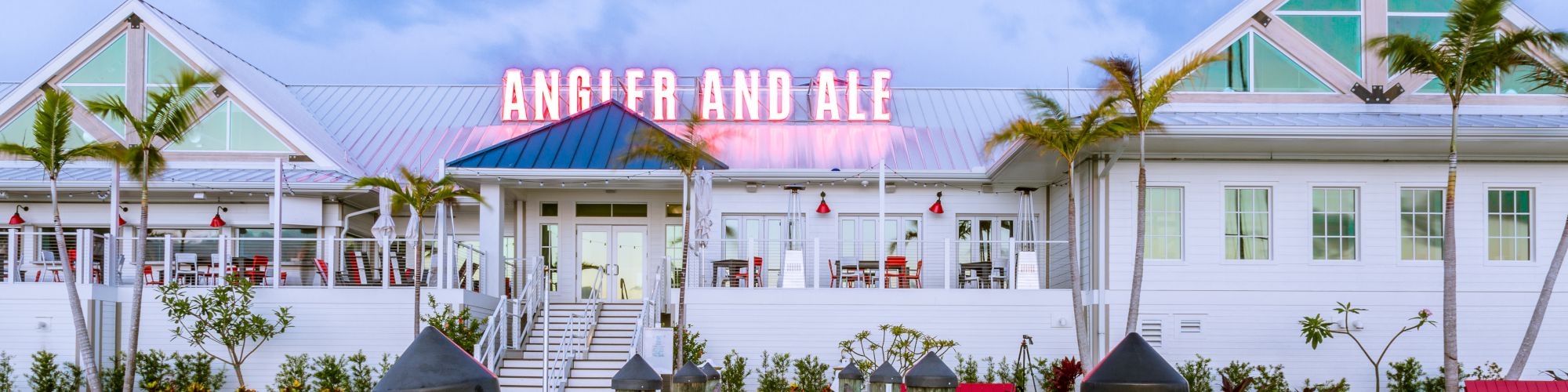 A waterfront restaurant named "Angler and Ale" with palm trees, dock, and reflection in the water, seen in the image.