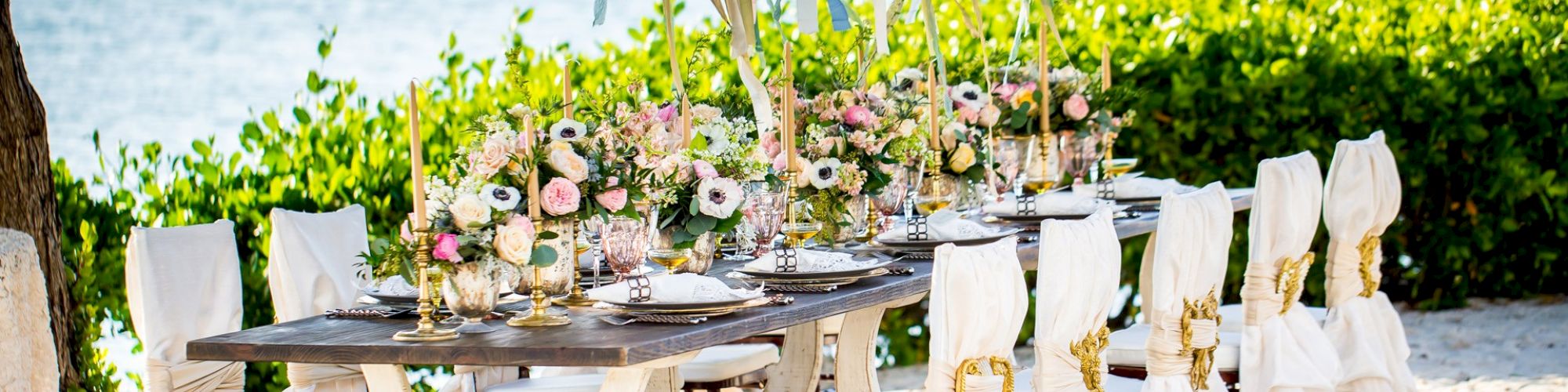 An elegant, outdoor dining setup with a decorated table, chairs, and elaborate floral arrangements near a waterfront, perfect for a special occasion.