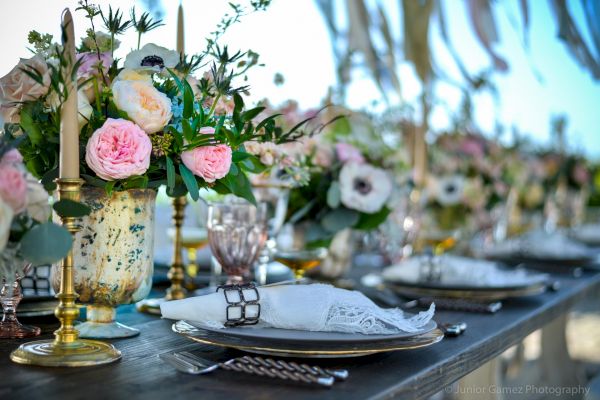 A beautifully set table with floral centerpieces, candles, and elegant dishware in an outdoor setting.