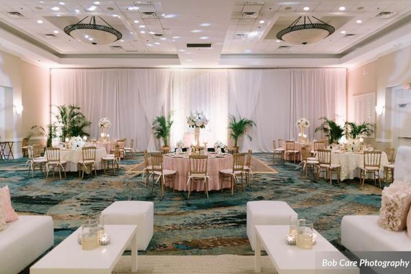 A beautifully decorated banquet hall with round tables, elegant chairs, floral centerpieces, and soft lighting, perfect for a special event.