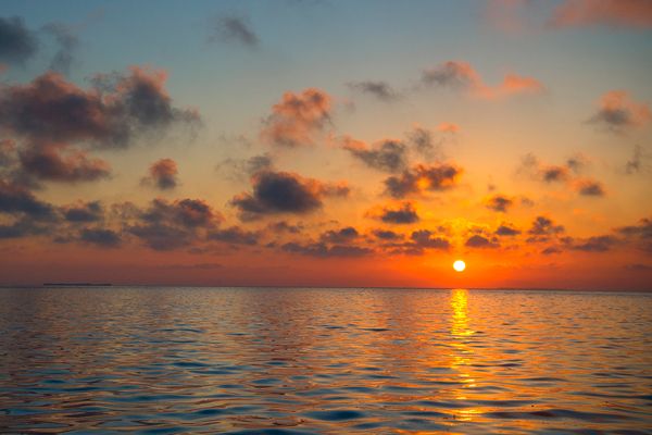 A serene ocean view with a colorful sunset, casting a warm reflection on the water and scattered clouds adding to the picturesque scene.