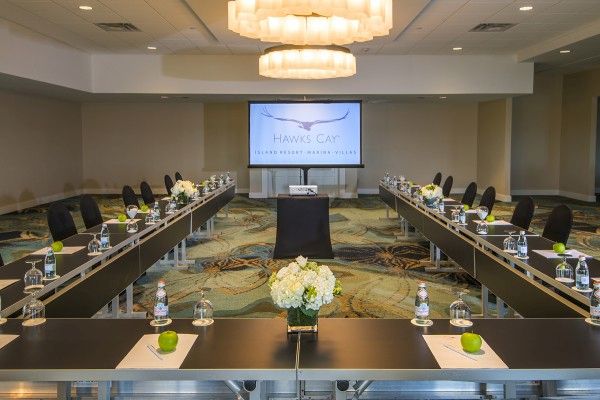 A conference room set up in a U-shape with a screen displaying "Hawks Cay," decorated with water bottles, green apples, and floral centerpieces.