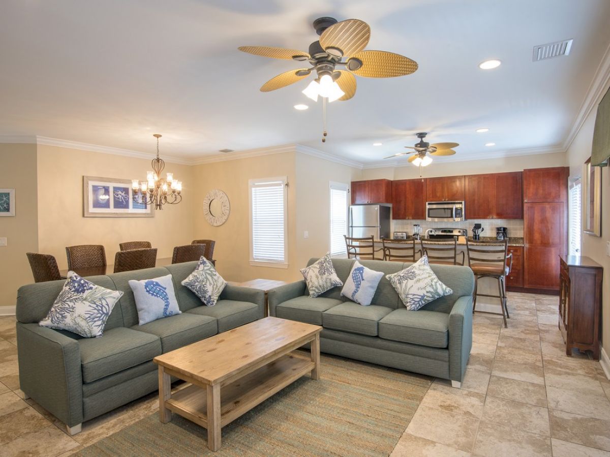 A cozy living room with two gray sofas, a wooden coffee table, and a kitchen with stainless steel appliances in the background.