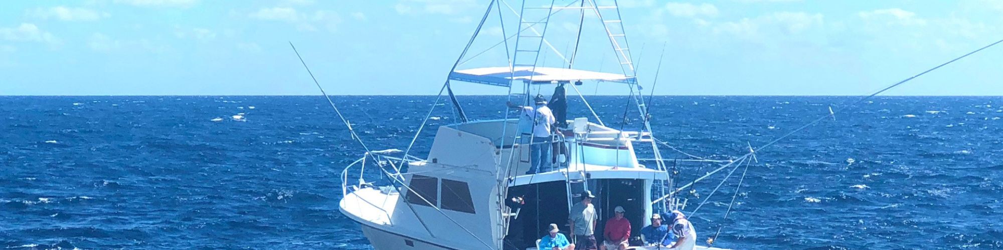 The image shows a white fishing boat named "Capullo" on the open sea with several people on board under a partly cloudy sky.