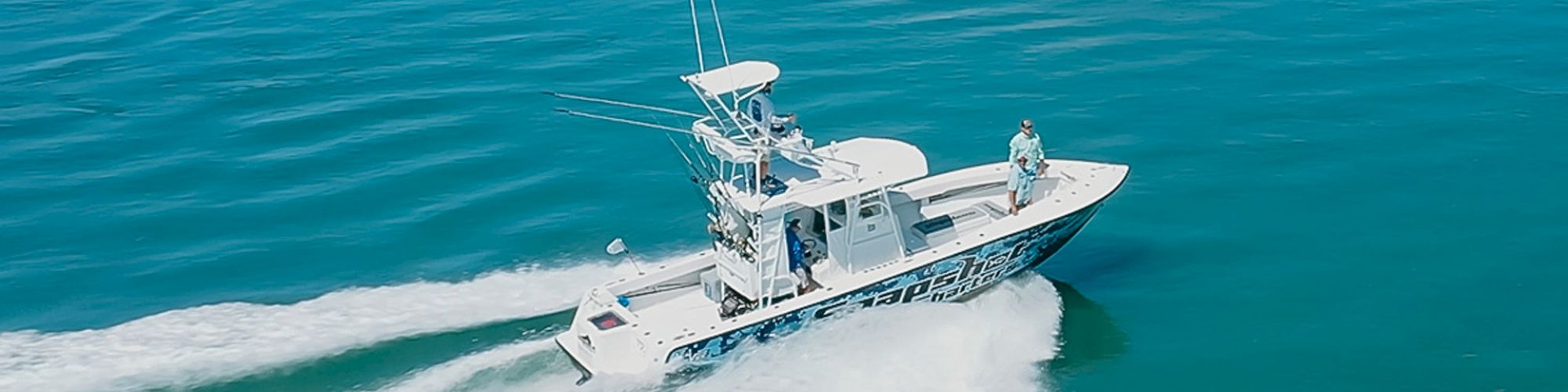 A boat speeds across the blue water, leaving a wake behind it. There are people on board enjoying the ride in the sunny weather.