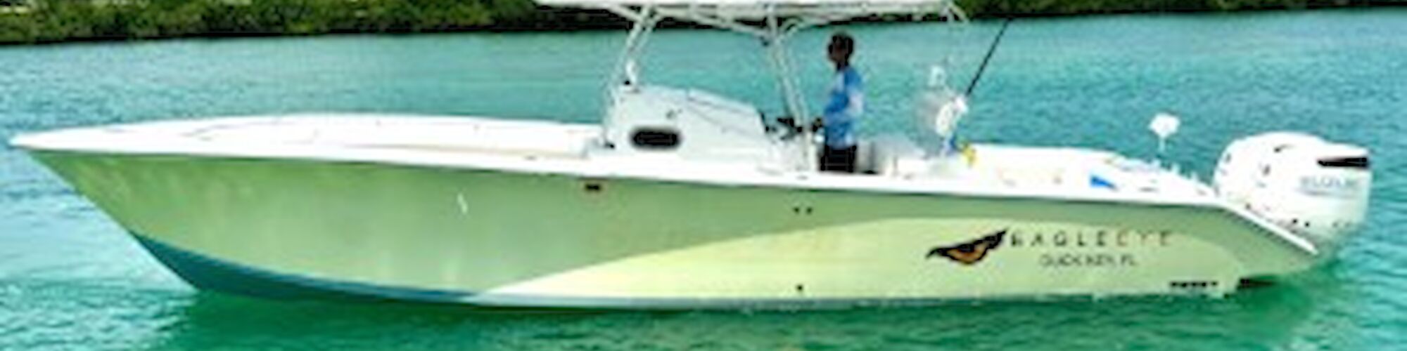 A white boat with "EAGLE EYE" written on the side is on a turquoise body of water under a partly cloudy sky.