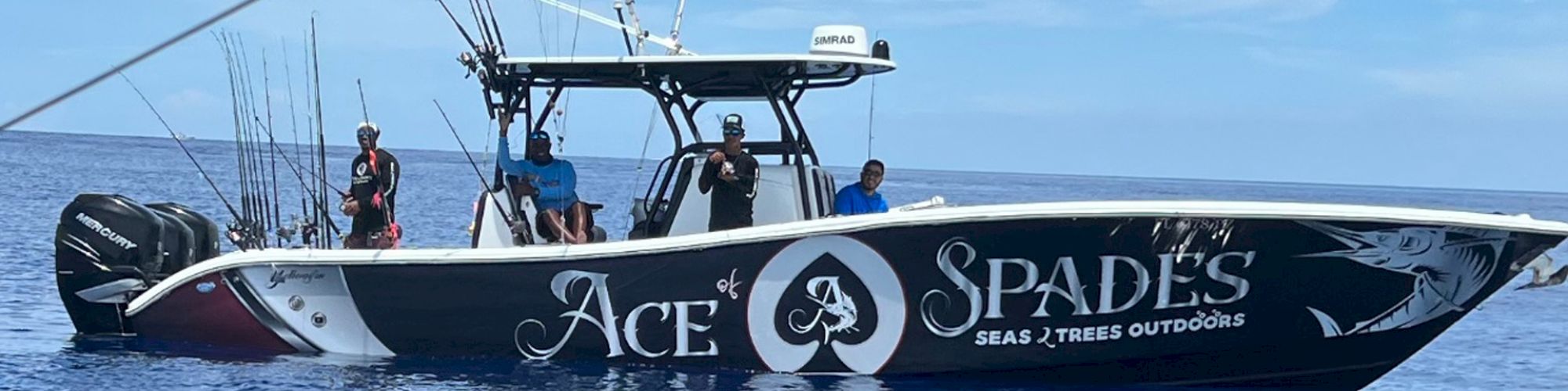 A boat named "Ace of Spades" with people on board, equipped with fishing rods, is on open water under a clear sky.