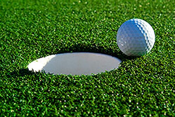 A golf ball is resting on the edge of a hole on a green field, moments away from potentially falling in.