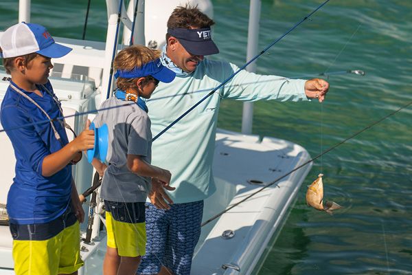 Three people on a boat are fishing; one of them is holding up a small fish on a line. They appear to be enjoying a day out on the water.