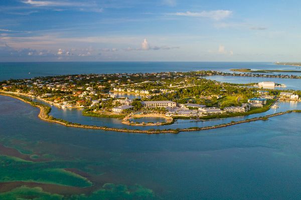 The image shows an aerial view of a coastal town or island, surrounded by water with buildings, greenery, and some infrastructure visible.