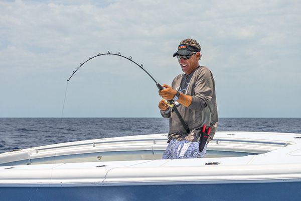 A person is standing on a boat and fishing, holding a bent fishing rod with the ocean in the background, and looking happy.