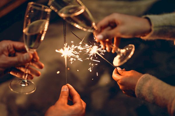 Four hands are holding sparklers and clinking champagne glasses, creating a festive atmosphere.