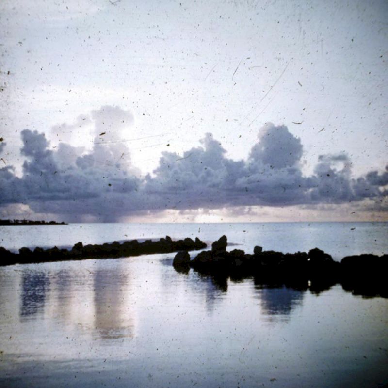 The image features a serene waterscape with calm water, rocky formations, and a cloudy sky reflecting on the water, creating a peaceful ambiance.