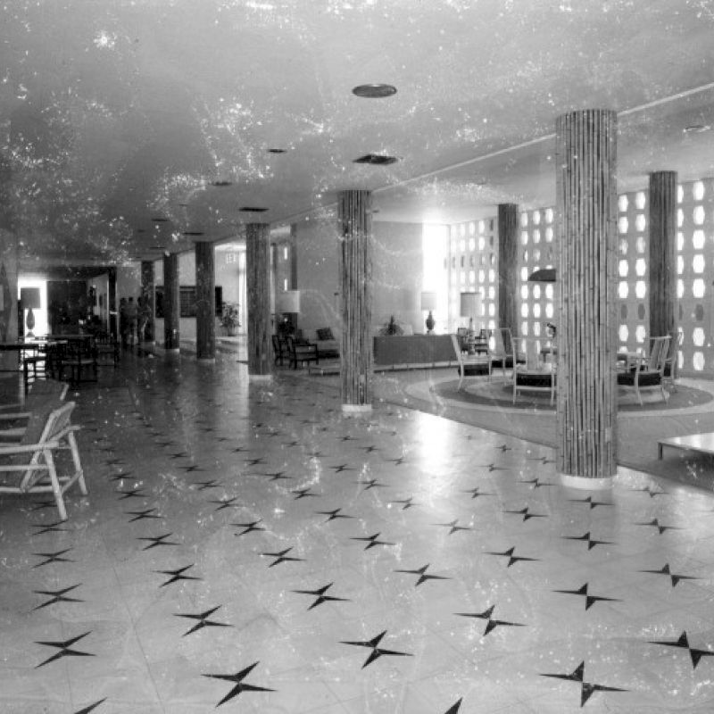 A vintage hotel lobby with star-patterned flooring, columns, and mid-century modern furniture, captured in black and white.