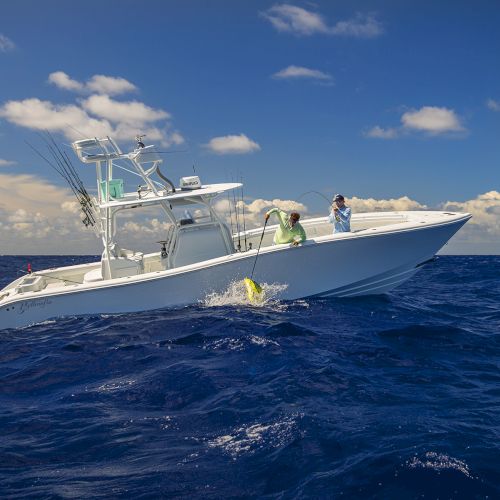 A white motorboat with people on board travels across a deep blue ocean under a partly cloudy sky.