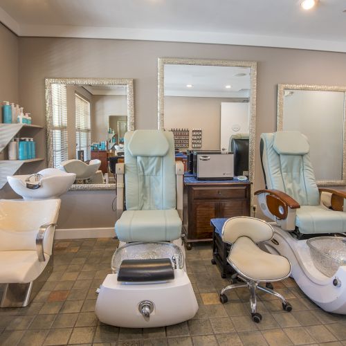 A modern salon with two spa chairs, a shampoo station, and large mirrors. The setting is well-lit and clean, ready for clients.