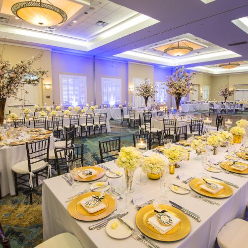 The image shows a beautifully decorated banquet hall with tables set for a formal event, featuring elegant table settings, flowers, and lighting.