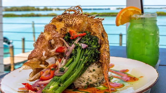 A whole cooked fish with vegetables and rice is served on a plate, paired with a green drink garnished with an orange slice.