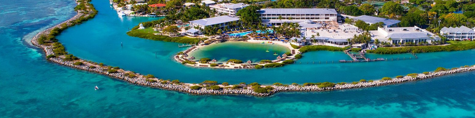 Aerial view of a coastal resort with turquoise waters, beaches, buildings, and lush greenery, showcasing a serene island destination.