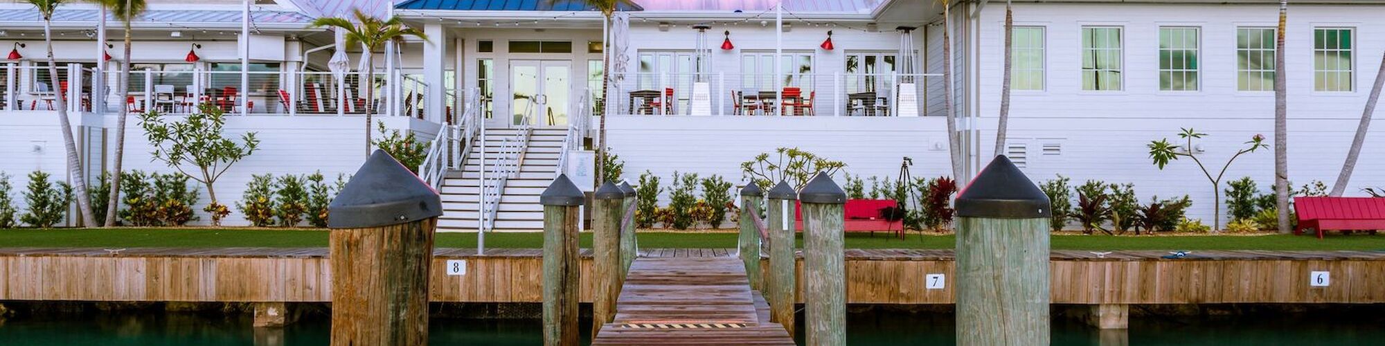 The image shows a waterfront restaurant named "Angler and Ale" with a wooden dock leading up to it, surrounded by palm trees.