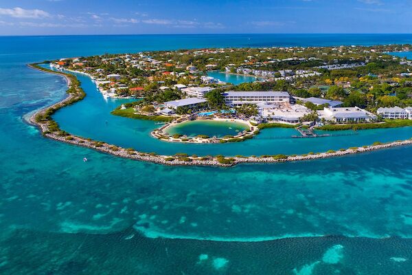 Aerial view of a lush island surrounded by turquoise waters, featuring buildings, beaches, and vibrant vegetation.