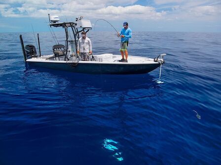 Two people are on a small fishing boat in calm, deep blue ocean waters, with one person holding a fishing rod.