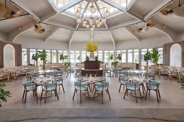 A spacious restaurant with elegant decor, featuring light blue chairs, wooden tables, and large windows allowing natural light to flood in.