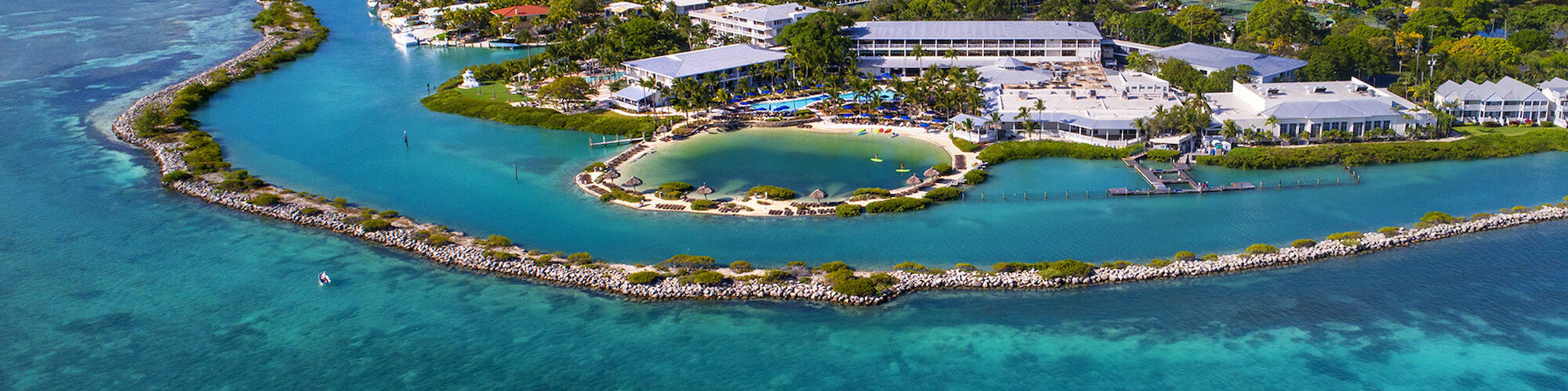 An aerial view of a picturesque coastal settlement surrounded by turquoise waters, featuring a mix of buildings and lush greenery.