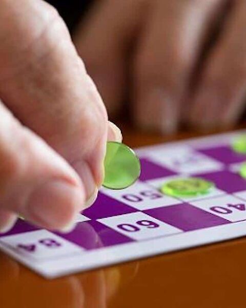 A hand places a green marker on a bingo card with numbers, on a wooden table.