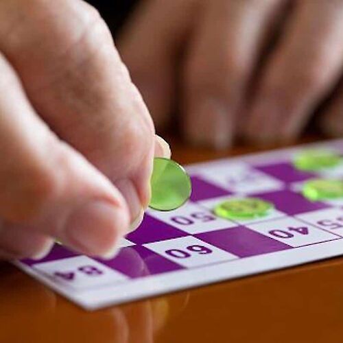 A hand places a green marker on a bingo card with numbers, on a wooden table.