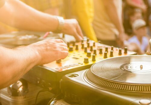 A DJ is mixing music on turntables and a mixer at an outdoor event.