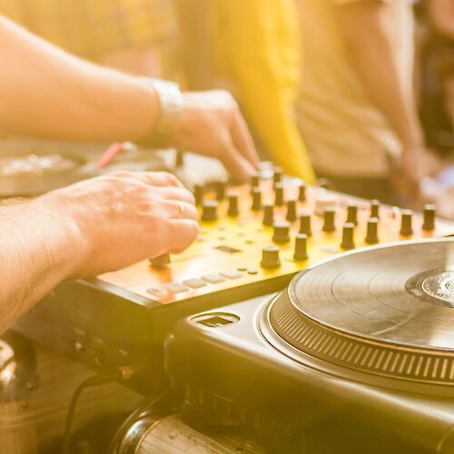 A DJ is mixing music on turntables and a mixer at an outdoor event.
