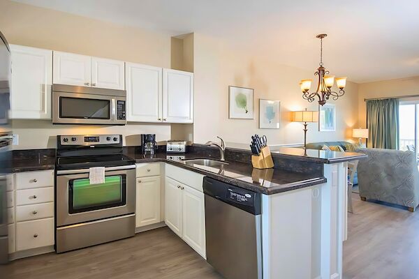 A modern kitchen with stainless steel appliances, white cabinets, and a nearby living area with a chandelier and seating.