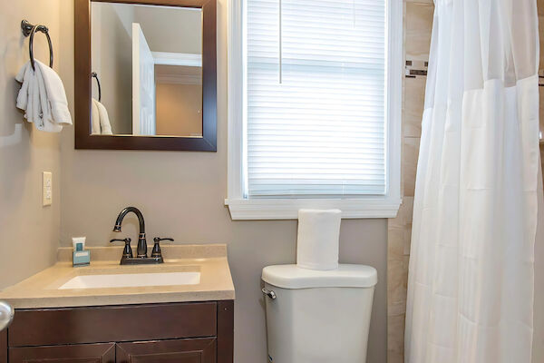 A bathroom with a sink, mirror, toilet, window, and a shower with a curtain.