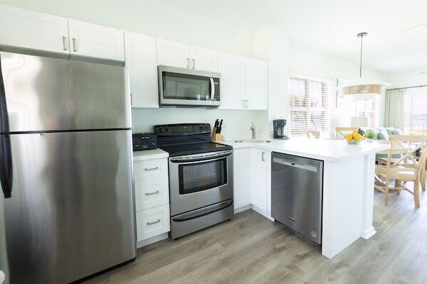 A modern kitchen with stainless steel fridge, oven, microwave, dishwasher, white cabinets, and a dining area with a fruit bowl.