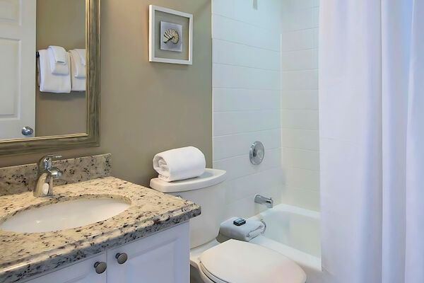 A bathroom with a granite countertop, sink, mirror, toilet, bathtub with shower curtain, towels, and wall art.