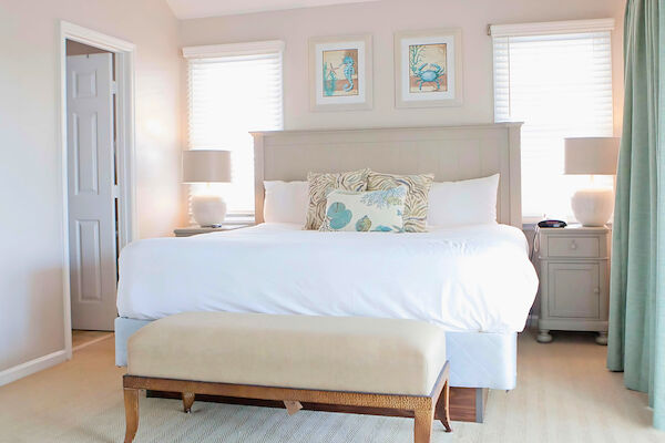 A cozy bedroom with a neatly made bed, two lamps, decorative pillows, and framed sea-themed artwork above the headboard.