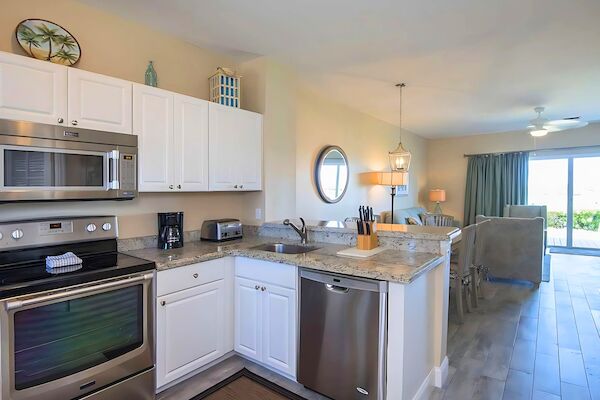 A modern kitchen with white cabinets, stainless steel appliances, and a cozy dining area with natural light from large windows.
