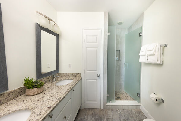 A modern bathroom with a granite countertop, dual sinks, a large mirror, glass shower, and neatly arranged towels.