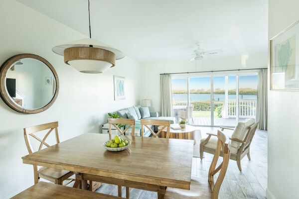 A bright living room with wooden furniture, a round mirror, and large glass doors overlooking a deck and scenic view.